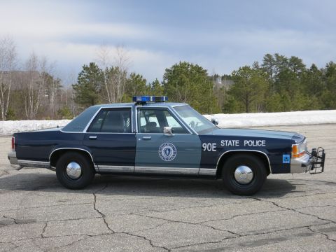 1991 Ford LTD Crown Victoria - blue Massachusetts State Police cruiser numbered 90E with a push bumper shown in profile against pine trees and snow.