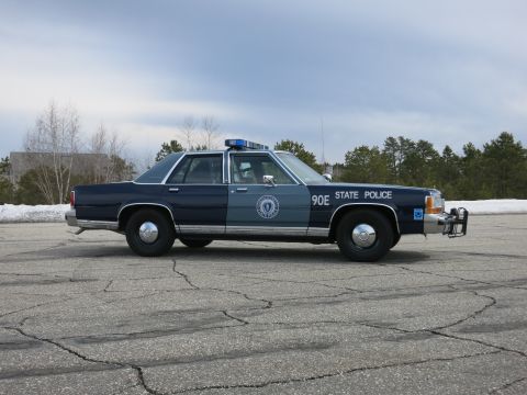 1991 Ford LTD Crown Victoria - blue Massachusetts State Police cruiser numbered 90E with a push bumper shown in profile against pines and snow.