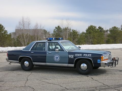 1991 Ford LTD Crown Victoria - Side view of a two-tone blue Massachusetts State Police sedan marked 90E with twin roof beacons and a push bumper.