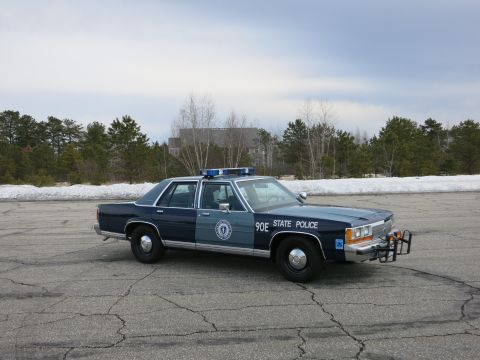 1991 Ford LTD Crown Victoria - two-tone blue State Police cruiser marked 90E sits at a three-quarter angle with its push bumper and lightbar on a snowy-edged lot.