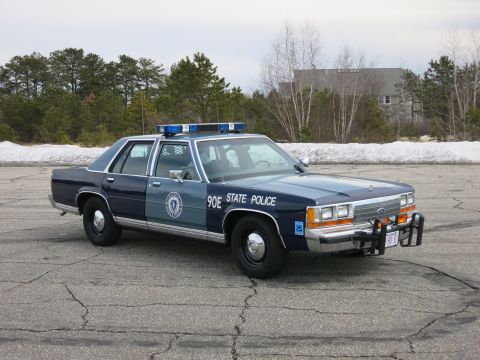 1991 Ford LTD Crown Victoria - two-tone blue State Police sedan marked 90E shown front three-quarter with a Ford grille, push bumper and red 90 E plate.