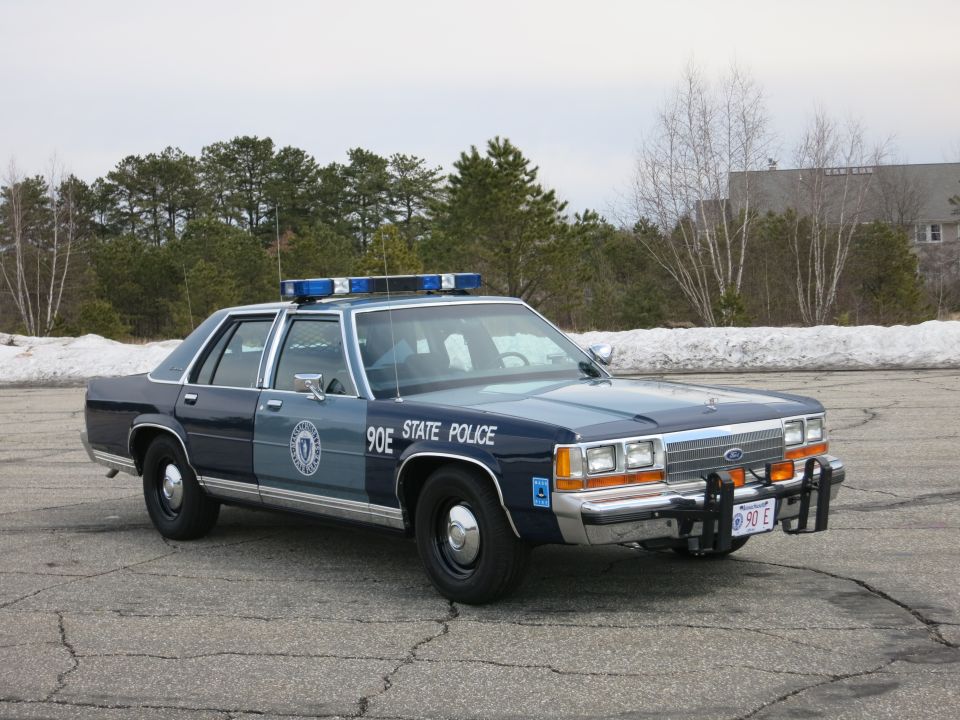 Two-tone blue State Police sedan, passenger front three-quarter, snow behind