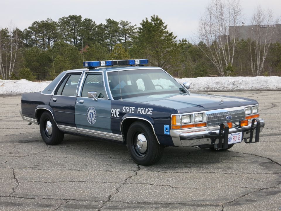 Blue State Police sedan, front three-quarter, push bumper and red 90 E plate