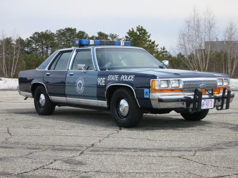 1991 Ford LTD Crown Victoria - two-tone blue State Police Ford sedan marked 90E shown front three-quarter, Ford oval on the grille and a red 90 E front plate.