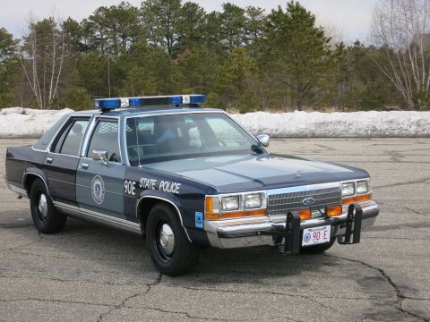 1991 Ford LTD Crown Victoria - Massachusetts State Police Ford LTD Crown Victoria with roof light bar and push bar, viewed from the front right near a snowbank.