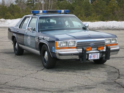 1991 Ford LTD Crown Victoria - Massachusetts State Police Ford cruiser with blue roof lights and push bumper, parked at a low front-right angle.