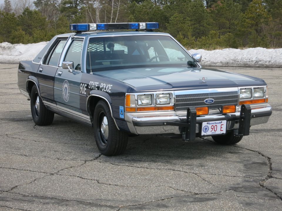 Two-tone blue Ford State Police sedan, front right view, snow in background