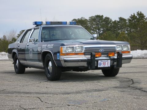 1991 Ford LTD Crown Victoria - two-tone blue Massachusetts State Police Ford LTD Crown Victoria photographed front-right with snow and pines behind.