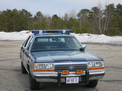 1991 Ford LTD Crown Victoria - two-tone blue Ford State Police sedan with blue roof lights and brush guard, viewed nearly head-on on a paved lot.