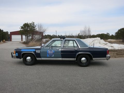 1991 Ford LTD Crown Victoria - Side profile of a two-tone blue Massachusetts State Police Ford sedan, unit 90E, with a NOT IN SERVICE placard on the door.