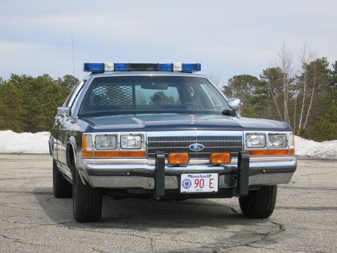 1991 Ford LTD Crown Victoria - two-tone blue Massachusetts State Police Ford LTD Crown Victoria viewed head-on with snow and pines in the background.
