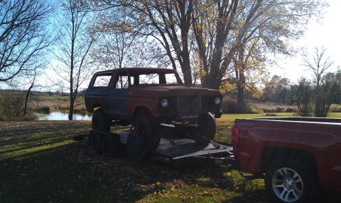 1978 Ford Bronco - Rusty 1978 Ford Bronco loaded onto a trailer, hitched to a red pickup truck.