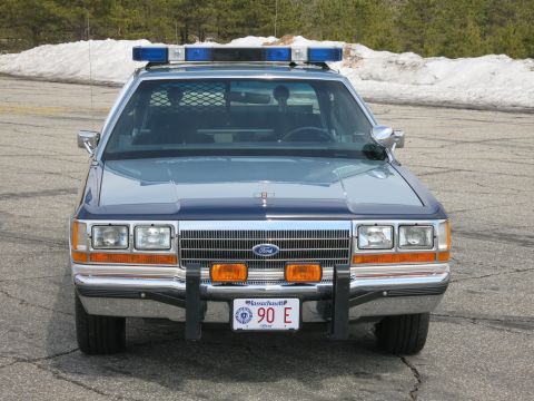 1991 Ford LTD Crown Victoria - two-tone blue Massachusetts State Police Ford LTD Crown Victoria viewed straight-on with snowbank and trees behind.