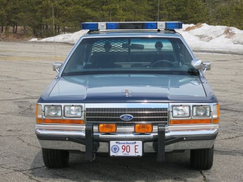 1991 Ford LTD Crown Victoria - blue Ford State Police sedan with blue roof light bar and push bar, photographed head-on near a snowbank.