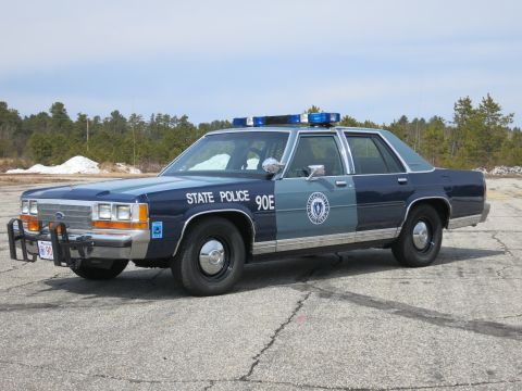 1991 Ford LTD Crown Victoria - Blue and gray Ford State Police cruiser displaying a round door seal and STATE POLICE 90E lettering, viewed from the side-front.