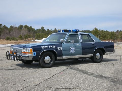 1991 Ford LTD Crown Victoria - Two-tone blue Ford State Police cruiser marked 90E with chrome push bumper and roof light bar, viewed front three-quarter.