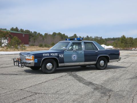 1991 Ford LTD Crown Victoria - Blue and gray Ford State Police sedan lettered 90E shown nearly in profile, with a round door seal and roof light bar.