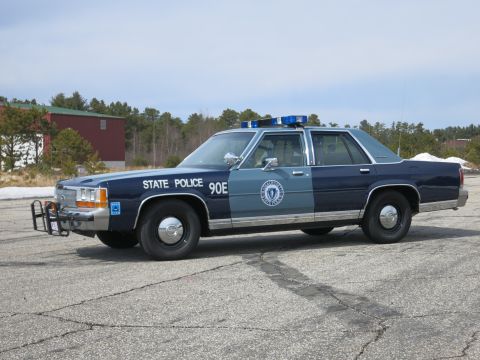1991 Ford LTD Crown Victoria - Blue and gray Ford State Police cruiser shown in side profile, lettered 90E with roof light bar and round door seal.