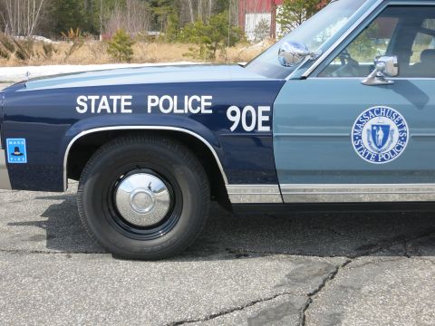 1991 Ford LTD Crown Victoria - Close-up of a blue police car door showing the round Massachusetts State Police seal, STATE POLICE 90E lettering and a Mass Pike sticker.
