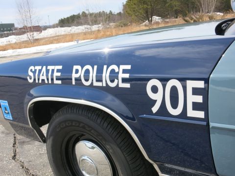 1991 Ford LTD Crown Victoria - Angled close-up of a dark-blue police car fender and door lettered STATE POLICE 90E with chrome trim and a Mass Pike sticker.