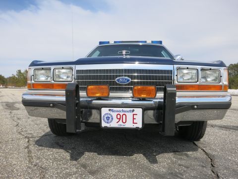 1991 Ford LTD Crown Victoria - Head-on front view of a blue Ford police sedan with chrome grille, black push bumper, light bar and a Massachusetts 90 E plate.