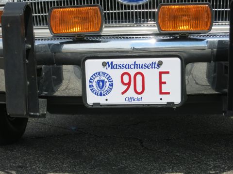 1991 Ford LTD Crown Victoria - Close-up of a white Massachusetts Official license plate reading 90 E with a State Police seal, mounted on a chrome bumper and push bar.