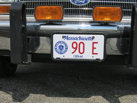 1991 Ford LTD Crown Victoria - Close-up of a Massachusetts Official license plate reading 90 E with State Police seal, below a Ford grille and amber turn lights.