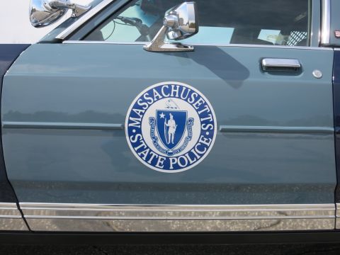 1991 Ford LTD Crown Victoria - Close-up of the round Massachusetts State Police seal decal on the gray-blue front door of a police car.