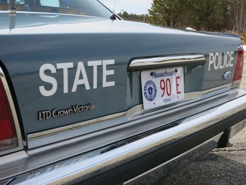 1991 Ford LTD Crown Victoria - Rear quarter of a gray Ford LTD Crown Victoria police car with STATE POLICE lettering and a Massachusetts Official plate reading 90 E.