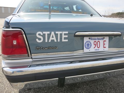 1991 Ford LTD Crown Victoria - Left rear corner of a gray Ford LTD Crown Victoria police car showing STATE lettering, taillight, and a Massachusetts 90 E plate.