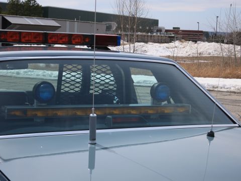 1991 Ford LTD Crown Victoria - Police car roof lightbar above the rear window with a row of amber lights and two blue takedown lamps, antenna at center.
