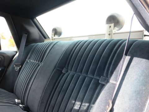 1991 Ford LTD Crown Victoria - Pleated blue cloth rear bench seat backed by a partition fitted with two speakers inside a car.