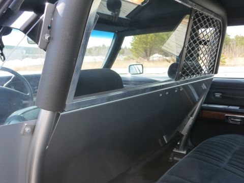 1991 Ford LTD Crown Victoria - Close view of a police car prisoner partition with a mesh upper window and folding panel over the blue cloth seats.
