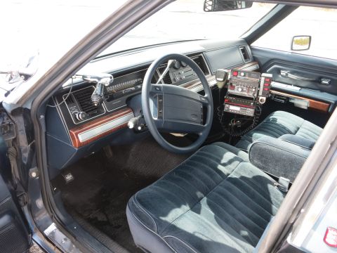 1991 Ford LTD Crown Victoria - Driver-side interior of a police car with steering wheel, woodgrain dashboard, blue cloth seats, and a center radio console.