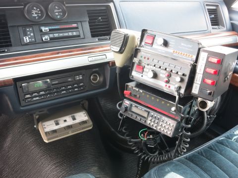 1991 Ford LTD Crown Victoria - Police car center area with a cassette stereo, Whelen siren controls, hand microphone, and a two-way radio.