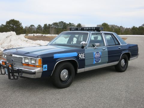 1991 Ford LTD Crown Victoria - Front-quarter view of a two-tone blue and black Ford LTD Crown Victoria police car with a lit OUT OF SERVICE roof sign and push bar.