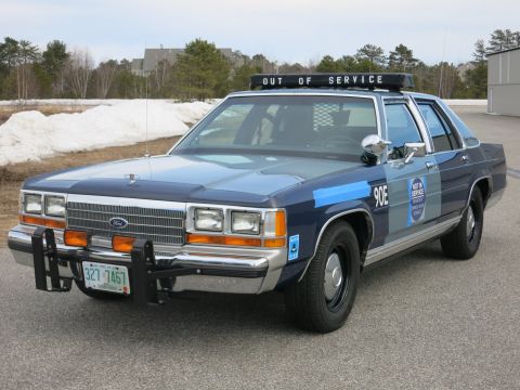 1991 Ford LTD Crown Victoria - Front view of a two-tone blue Ford LTD Crown Victoria police car with a chrome push bar, marked 90E and OUT OF SERVICE.