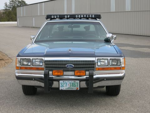 1991 Ford LTD Crown Victoria - Direct front view of a blue Ford police cruiser showing its grille, Ford emblem, push bumper, OUT OF SERVICE lightbar and New Hampshire pla…