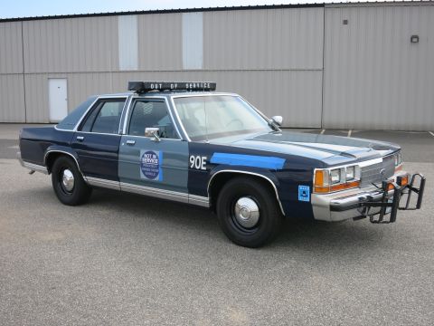 1991 Ford LTD Crown Victoria - Front-right three-quarter view of a two-tone blue Ford police cruiser marked 90E with NOT IN SERVICE door decal and push bumper.