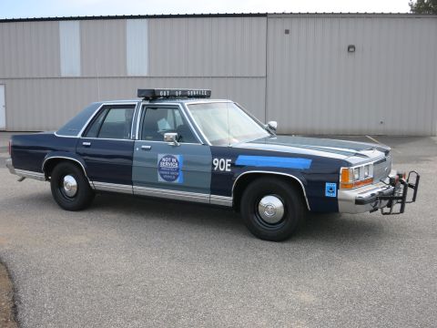 1991 Ford LTD Crown Victoria - Passenger-side view of a two-tone blue Ford LTD Crown Victoria police cruiser marked 90E with a NOT IN SERVICE door decal and push bumper.