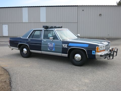 1991 Ford LTD Crown Victoria - Front-right three-quarter view of a two-tone blue Ford police cruiser marked 90E with a NOT IN SERVICE decal and push bumper on pavement.