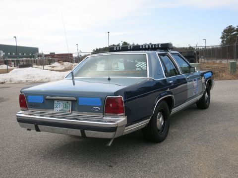 1991 Ford LTD Crown Victoria - Rear-right three-quarter view of a blue Ford LTD Crown Victoria police cruiser with OUT OF SERVICE lightbar and a New Hampshire plate.
