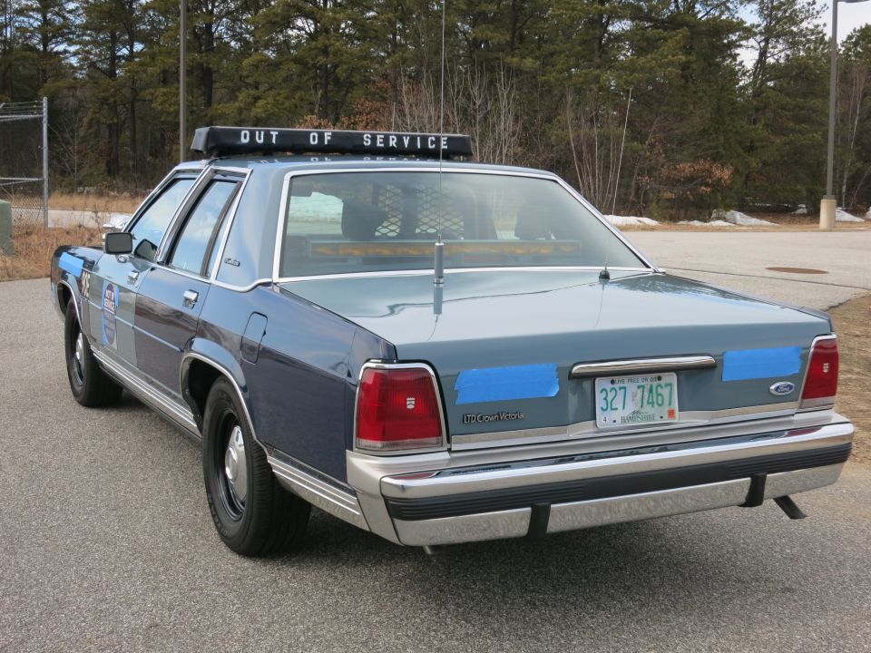 Rear-left view of blue Ford police sedan with OUT OF SERVICE lightbar