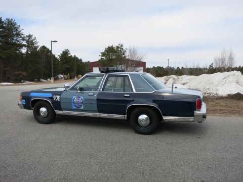 1991 Ford LTD Crown Victoria - Driver-side profile of a two-tone blue Ford LTD Crown Victoria police cruiser marked 90E parked on pavement near snow piles.
