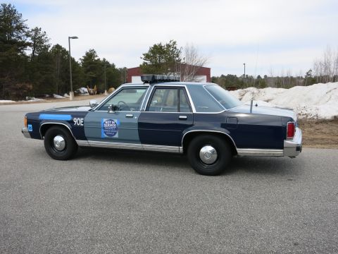 1991 Ford LTD Crown Victoria - Driver-side three-quarter view of a two-tone blue Ford LTD Crown Victoria police cruiser marked 90E with push bumper near snow piles.