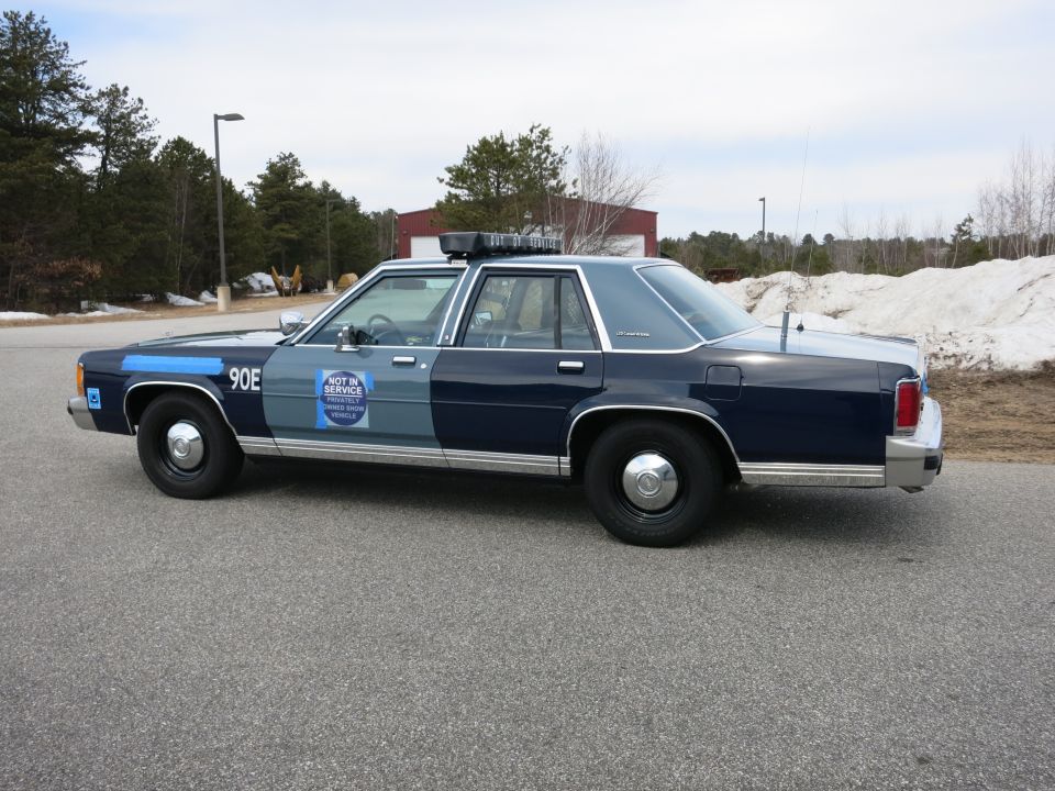 Driver-side view of blue Ford police cruiser marked 90E with push bumper
