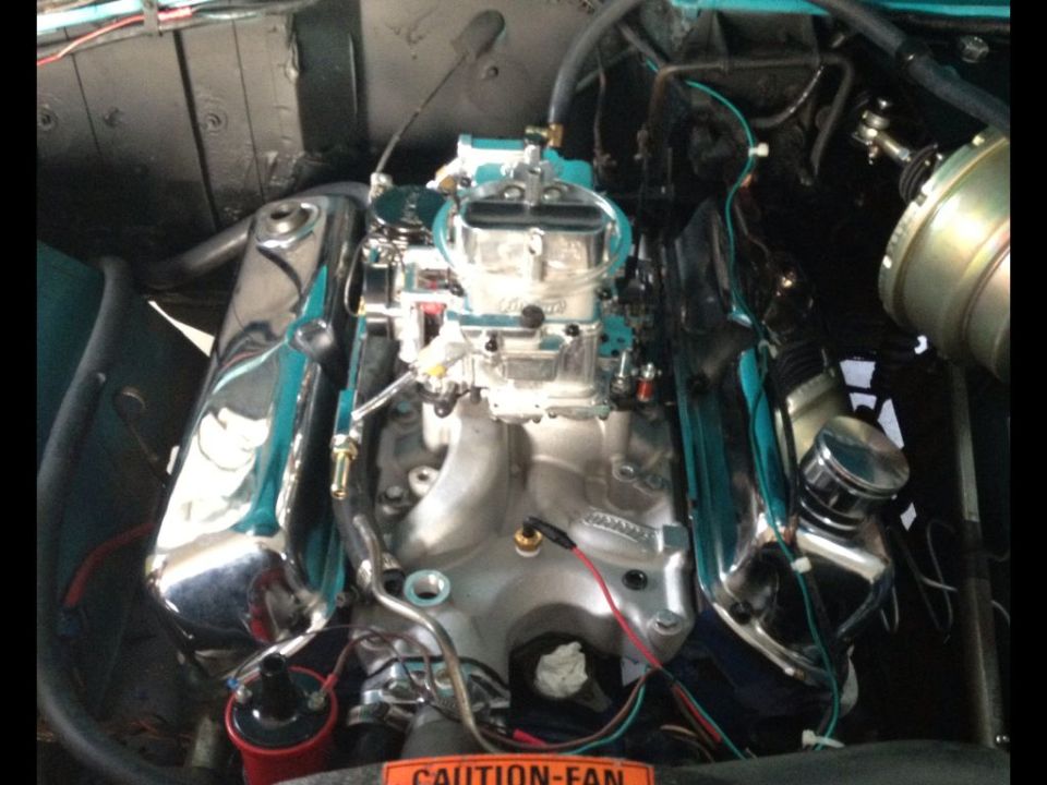 V8 engine with chrome valve covers and a Holley carburetor. "CAUTION-FAN" sticker visible