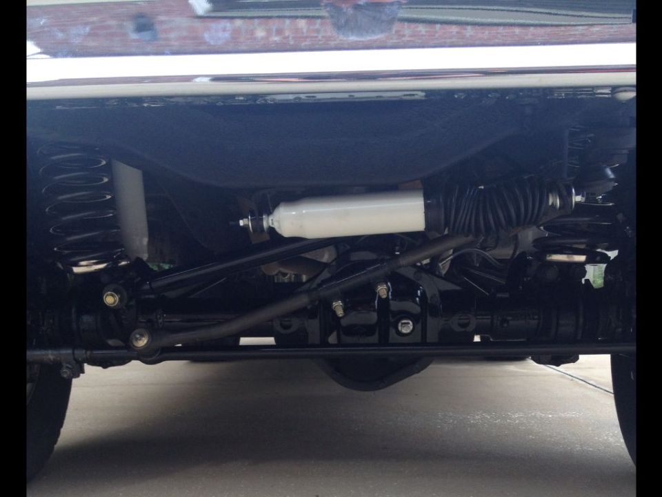 Undercarriage view of a vehicle's front suspension and steering components. Shows springs, shocks, and tie rods