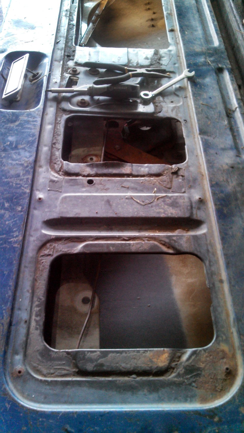 Interior of a blue car door panel with two large cutouts and tools on top