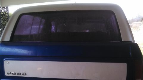 1979 Ford Bronco - The rear of a blue and white Ford Bronco shows a white tailgate panel and tinted rear window.